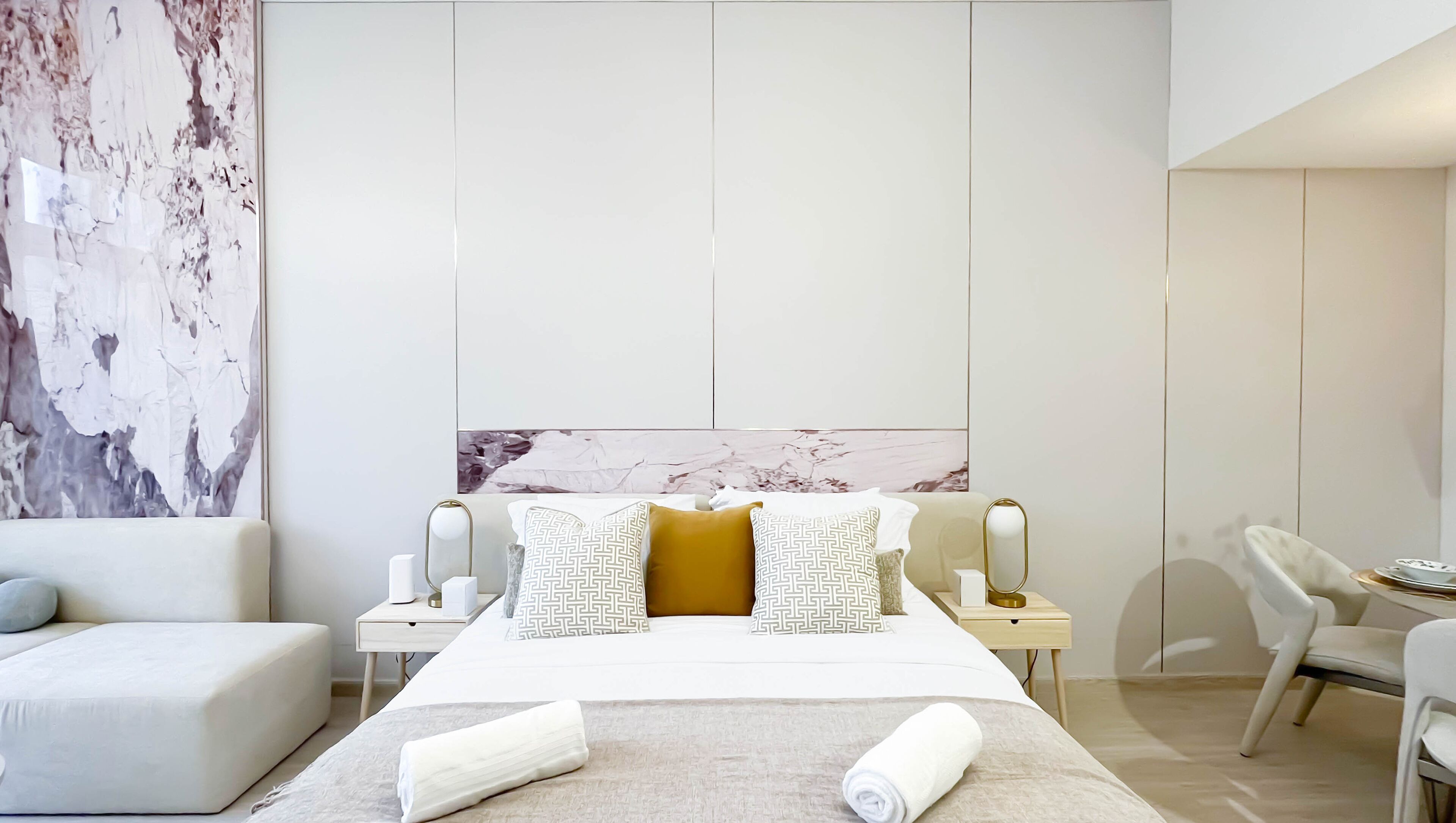 A modern hotel room with a large bed, a sofa, a desk with a chair, and a large abstract painting on the wall.