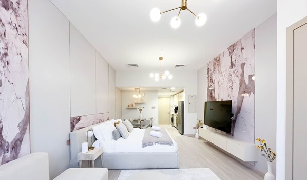 A modern hotel room with a large bed, a sofa, a TV, and a dining area in the background. - Stylish Ground-floor Studio JVC (Dubai)
