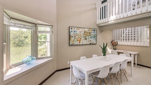 A dining area with a white table and chairs, a large window with blinds, a potted plant, and a wall-mounted artwork. - Spacious Home w/ Game Room, 2 Mi to Concord Mills! (Concord)