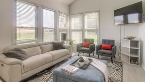 A living room with a beige sofa, two armchairs, a coffee table with a tray, a flat-screen TV, and a bookshelf. - Spacious Home w/ Game Room, 2 Mi to Concord Mills! (Concord)