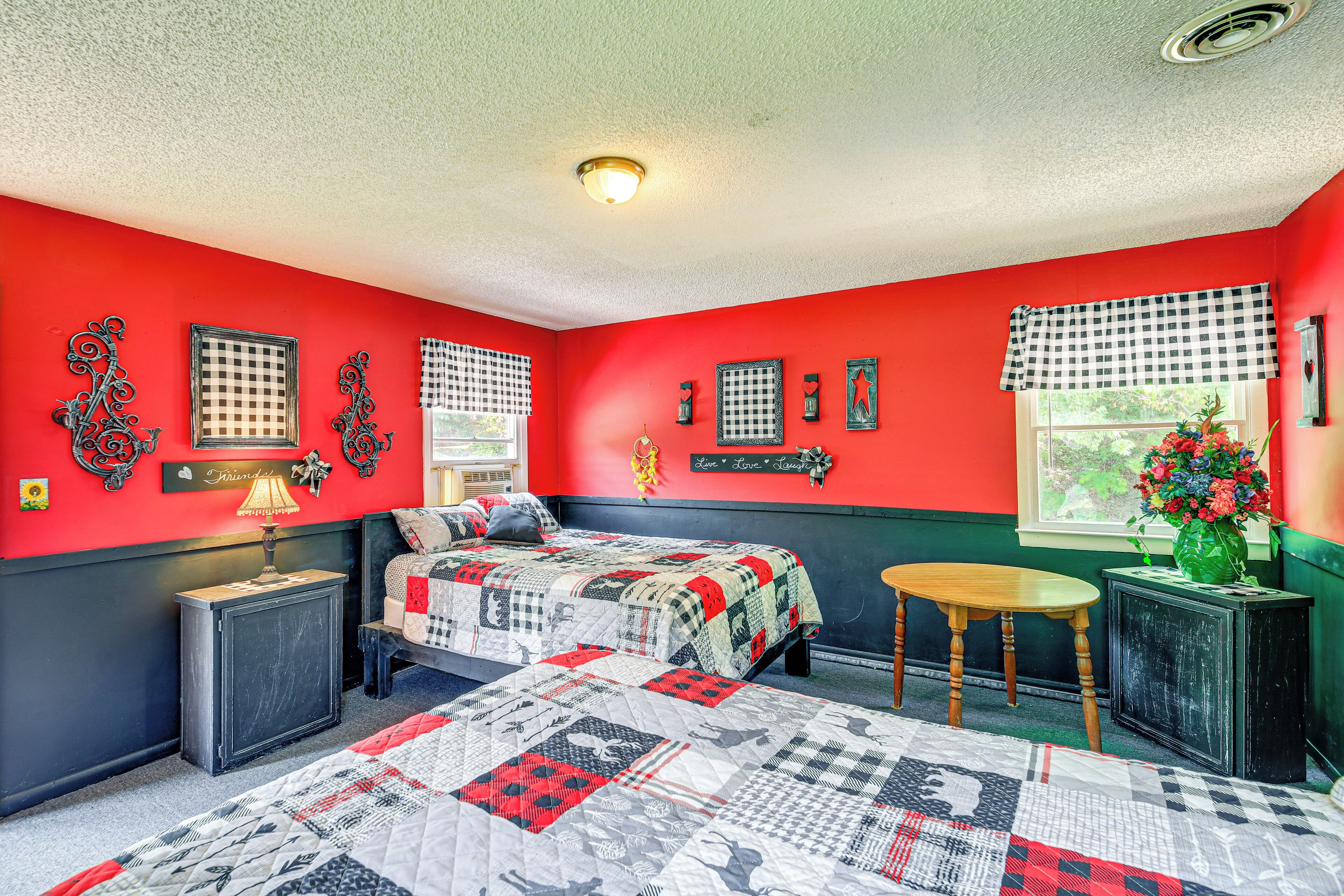 Un dormitorio con una paleta de colores rojo y negro, una cama con colcha, una mesita pequeña y una ventana con vistas a la vegetación.
