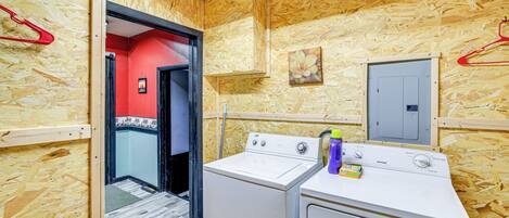 A laundry room with two washing machines, a red wall, and a wooden ceiling.