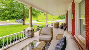 A covered porch with a sofa, chairs, and a table. - Renovated 1800s Brick Farmhouse in Granville (Granville)