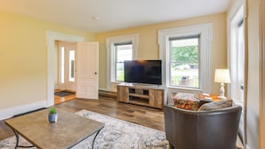 A living room with a flat-screen TV on a wooden stand, a gray sofa, a small table with a plant, and a patterned rug. - Renovated 1800s Brick Farmhouse in Granville (Granville)