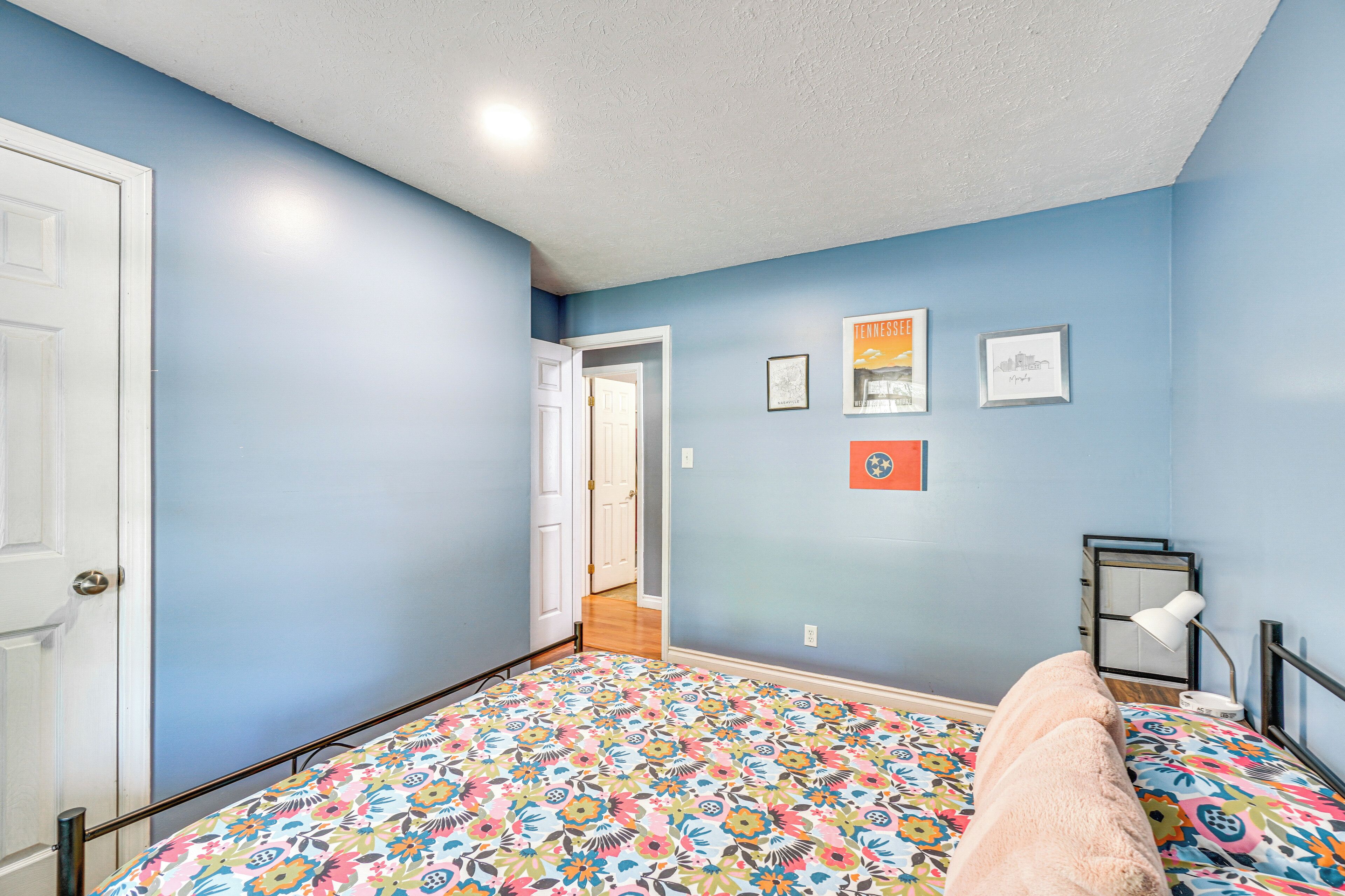 A bedroom with a floral bedspread, a white door, and a hallway leading to another room.