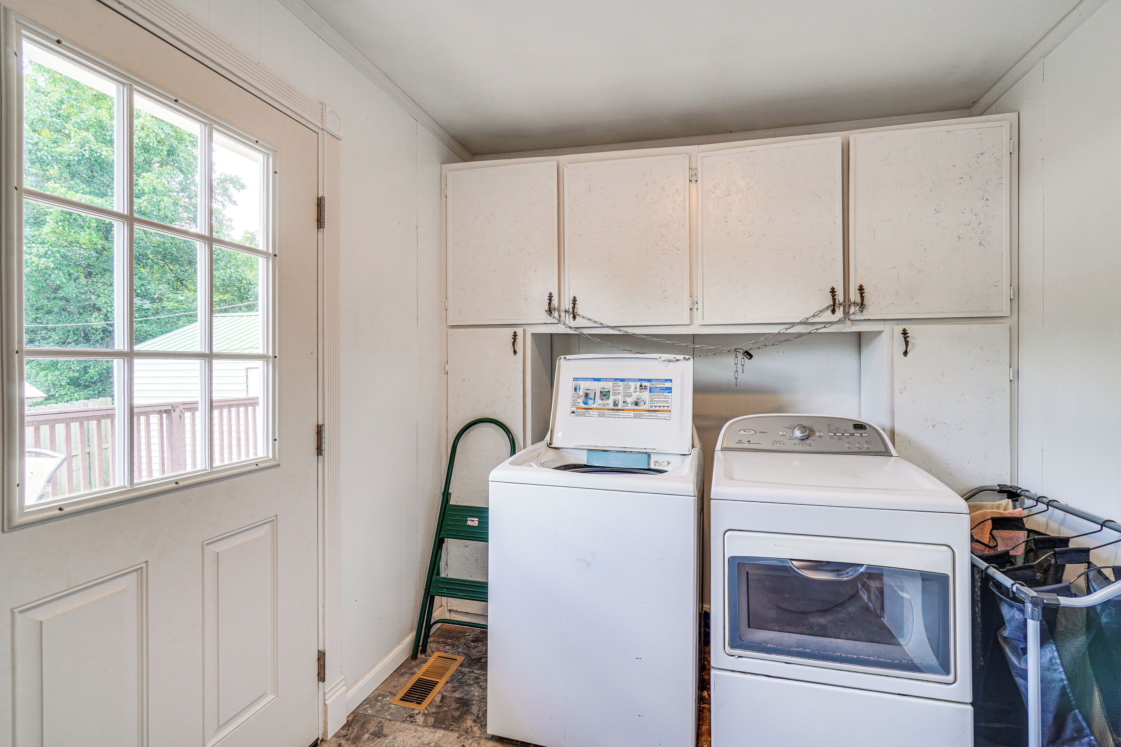 A laundry room with a washing machine and dryer, a window, and a green chair.