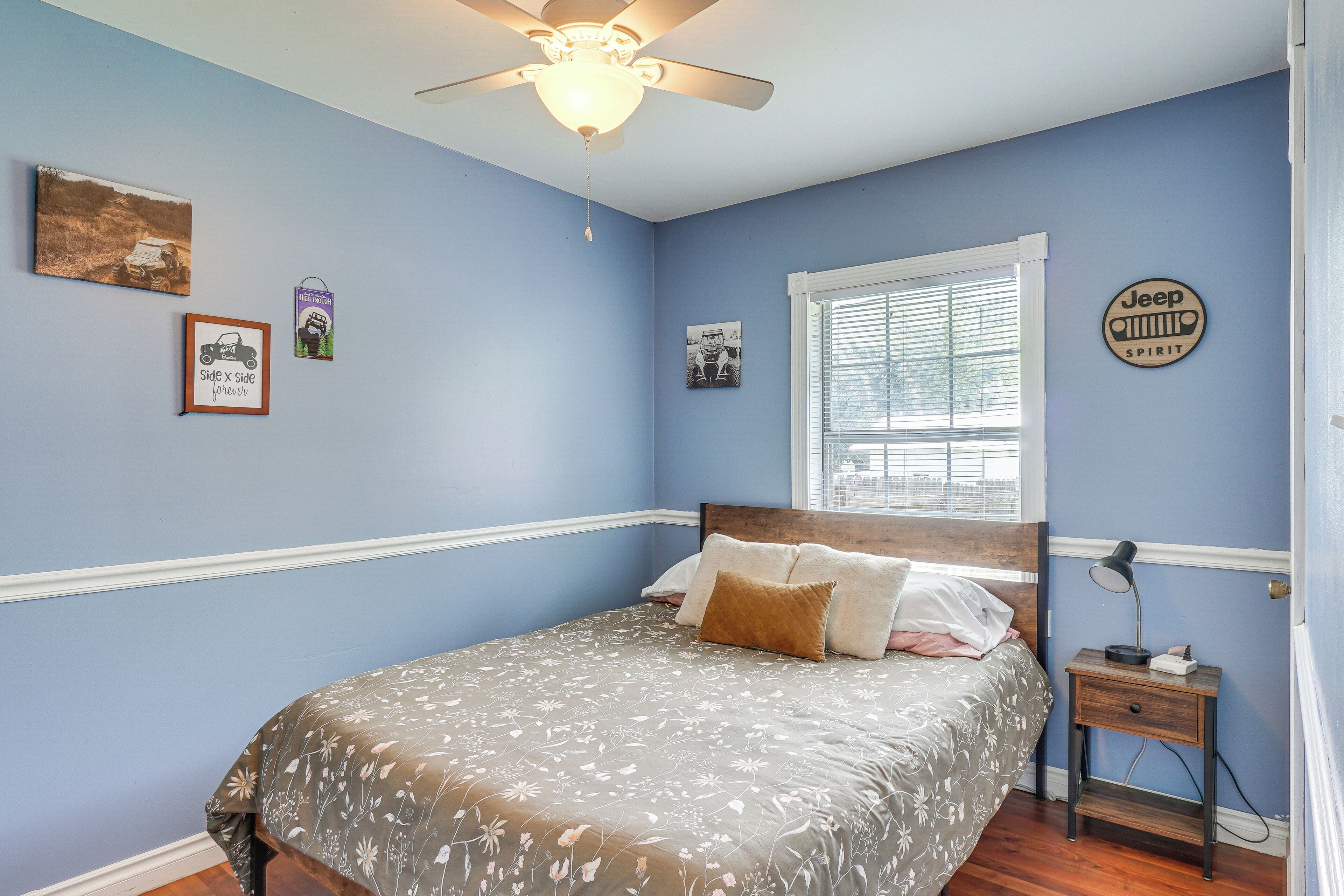 A bedroom with a bed, a nightstand, a ceiling fan, and wall decorations.