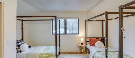 A room with two beds, a window, a small table with a lamp, and a ceiling light.