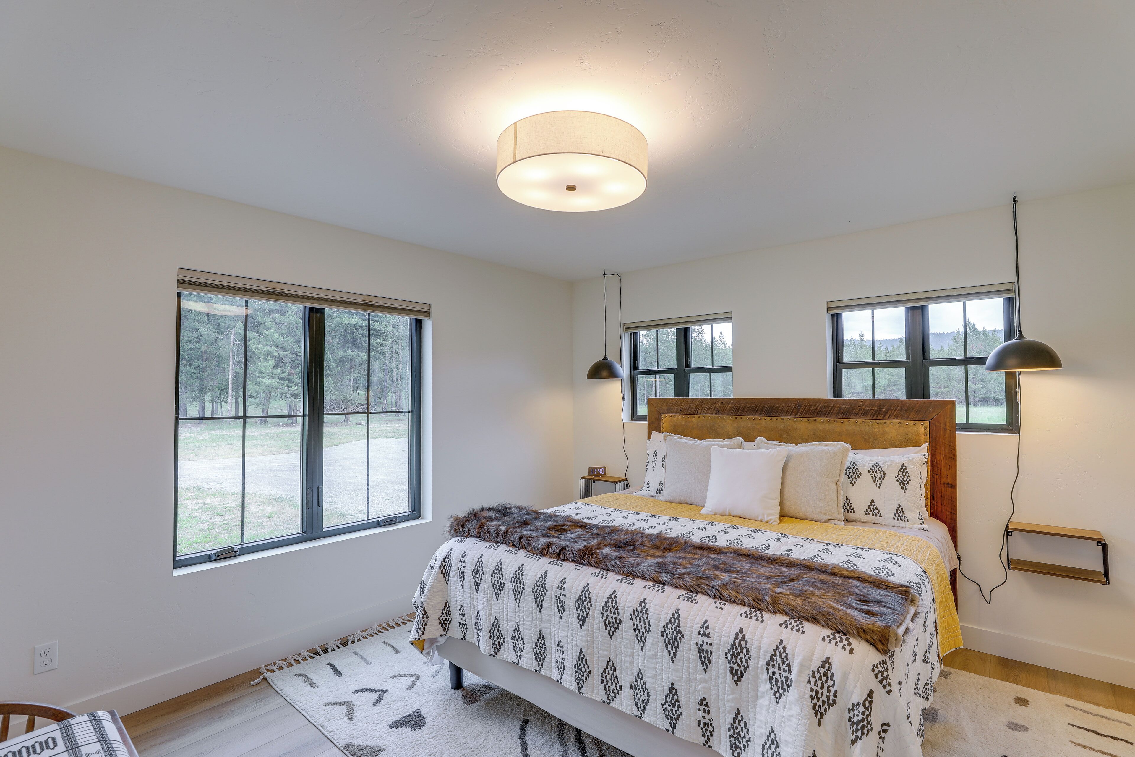 A bedroom with a large bed, two windows, a ceiling light, and a bedside table.