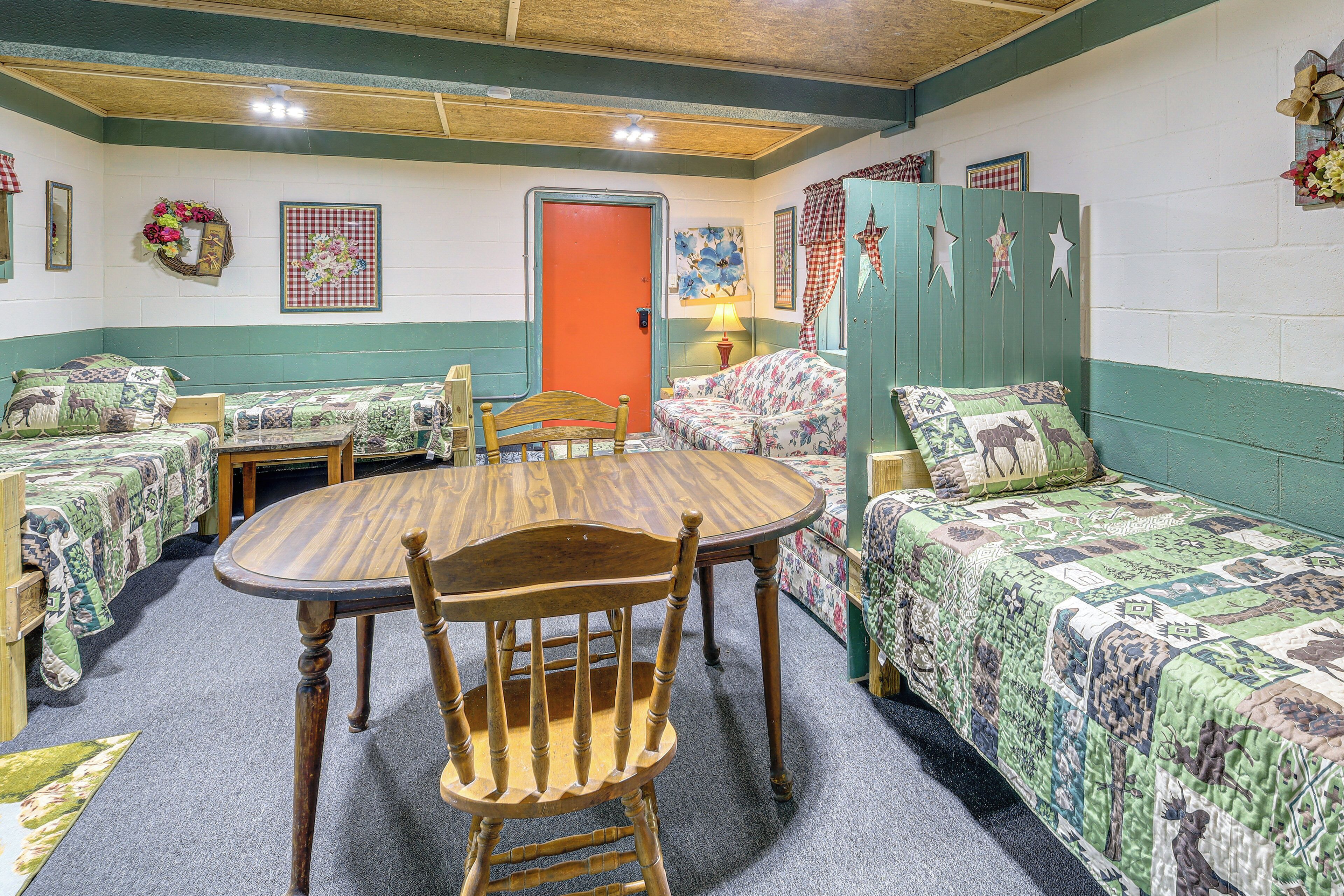 Una habitación con dos camas individuales, una mesa redonda de madera con sillas, y una puerta con marco rojo.