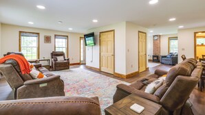 A spacious living room with multiple seating options, including a large sofa and chairs, a flat-screen TV mounted on the wall, and a fireplace. - Mountain & Sunset Views: Upstate Family Home (Granville)