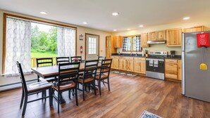 A modern kitchen with wooden cabinets, a stainless steel refrigerator, and a dining area with a wooden table and chairs. - Mountain & Sunset Views: Upstate Family Home (Granville)