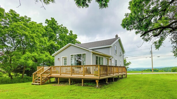 A two-story house with a wooden deck and a staircase leading to the entrance. - Mountain & Sunset Views: Upstate Family Home (Granville)