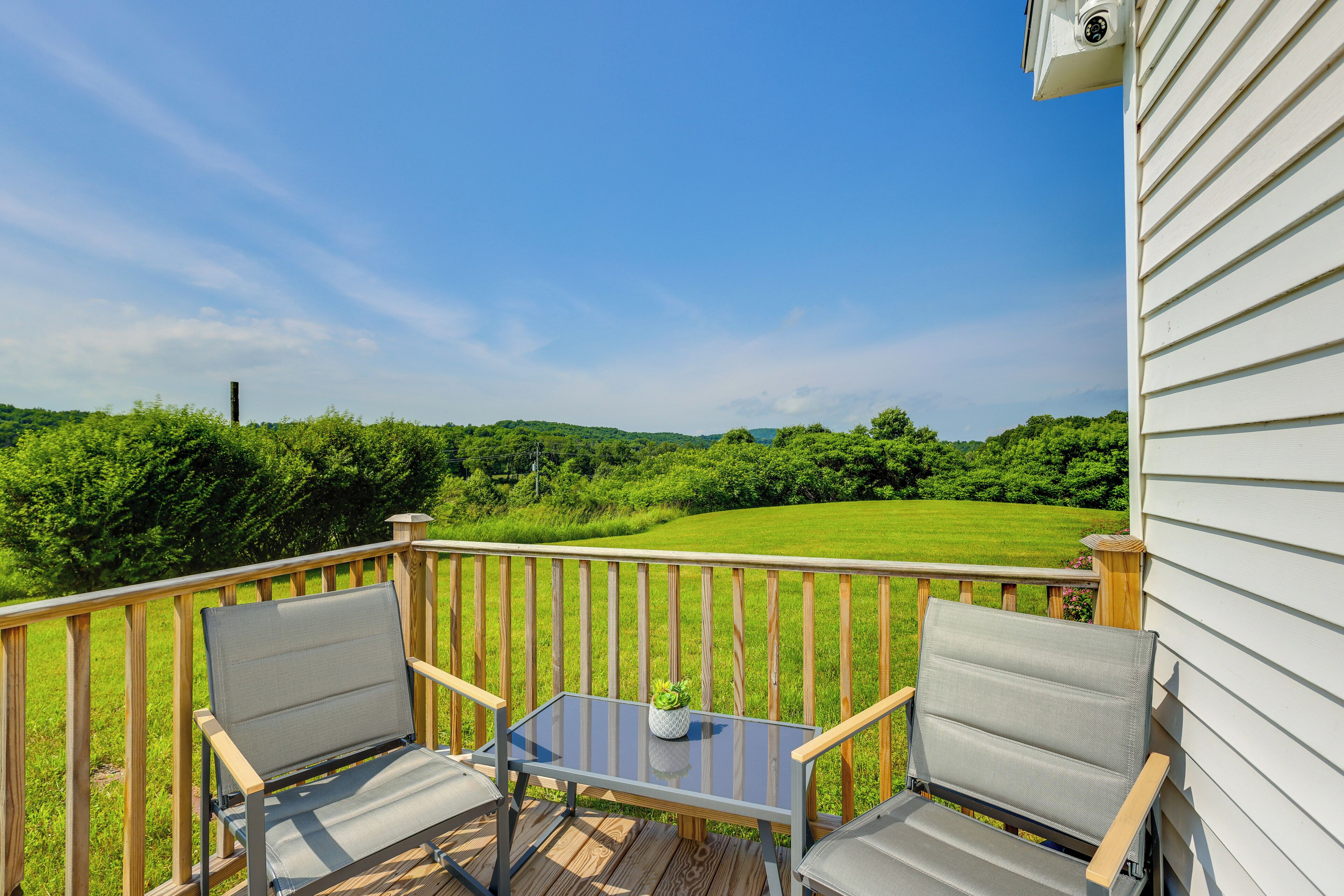 A wooden deck with two chairs and a small table, overlooking a green field and distant hills.
