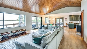Un espacio habitable amplio con techo de madera, ventanas grandes y una cocina al fondo.