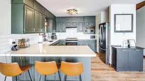 Una cocina moderna con armarios verdes, una isla grande con taburetes de bar, un horno empotrado y un refrigerador.