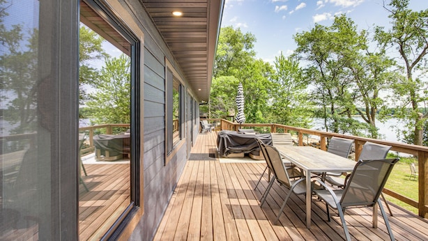 Una terraza de madera con una mesa y sillas, con vista a un lago y árboles.