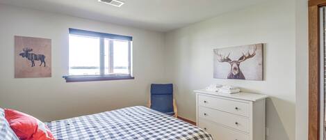 A bedroom with a checkered bedspread, a window with blinds, a desk with a telephone, and two wall-mounted animal paintings.