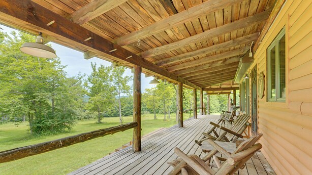 Una terraza de madera con zona cubierta, mobiliario exterior y vistas a un paisaje cubierto de césped.