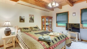 Un dormitorio acogedor con techo de madera, una cama con colcha temática de oso, un televisor sobre un mueble bajo y un armario con puerta de cristal.