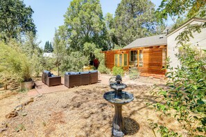 A backyard with a wooden deck, outdoor seating, a fountain, and a house with a sloped roof. - Wine Country Cottage in Historic Fiddletown! (Fiddletown)