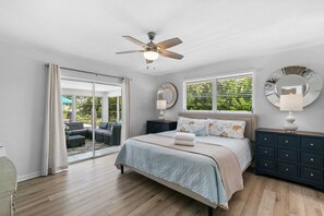 A bedroom with a large bed, a ceiling fan, a nightstand with a lamp, a dresser, and a sliding glass door leading to a patio area.