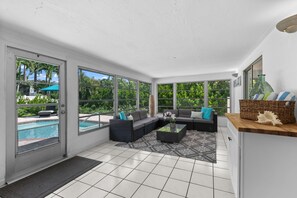 A sunlit room with a large window, a pool, a sofa, and a coffee table.