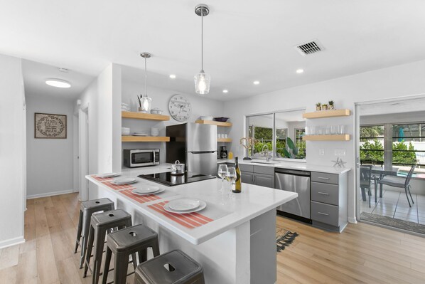 A modern kitchen with white countertops, stainless steel appliances, and a central island with bar stools.