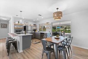 A modern kitchen with a central island, bar stools, and a dining table with chairs.