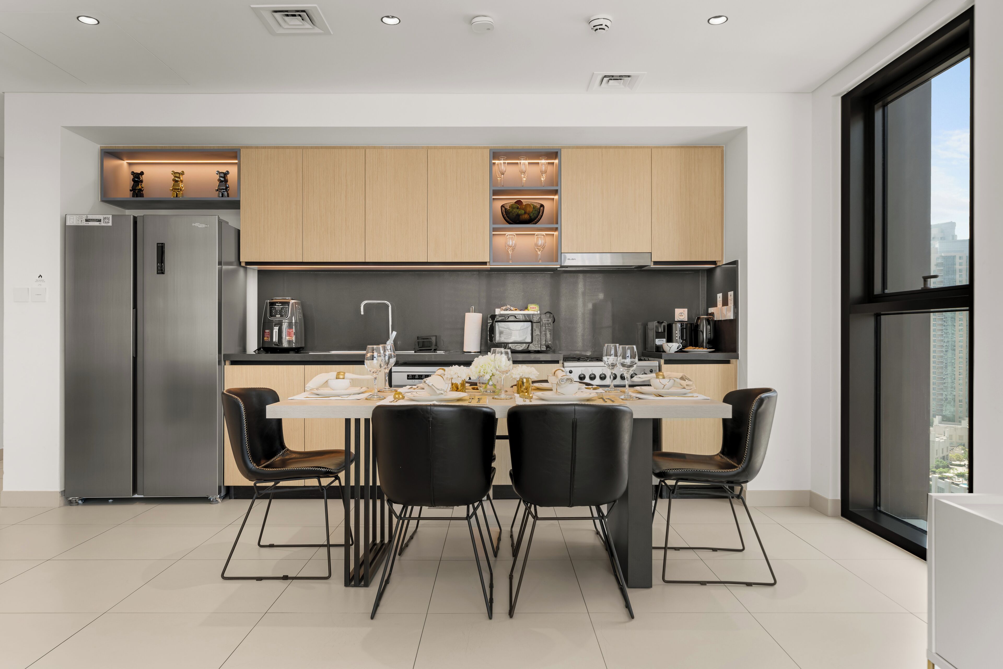 A modern kitchen with a dining area, stainless steel appliances, and a large window offering a city view.