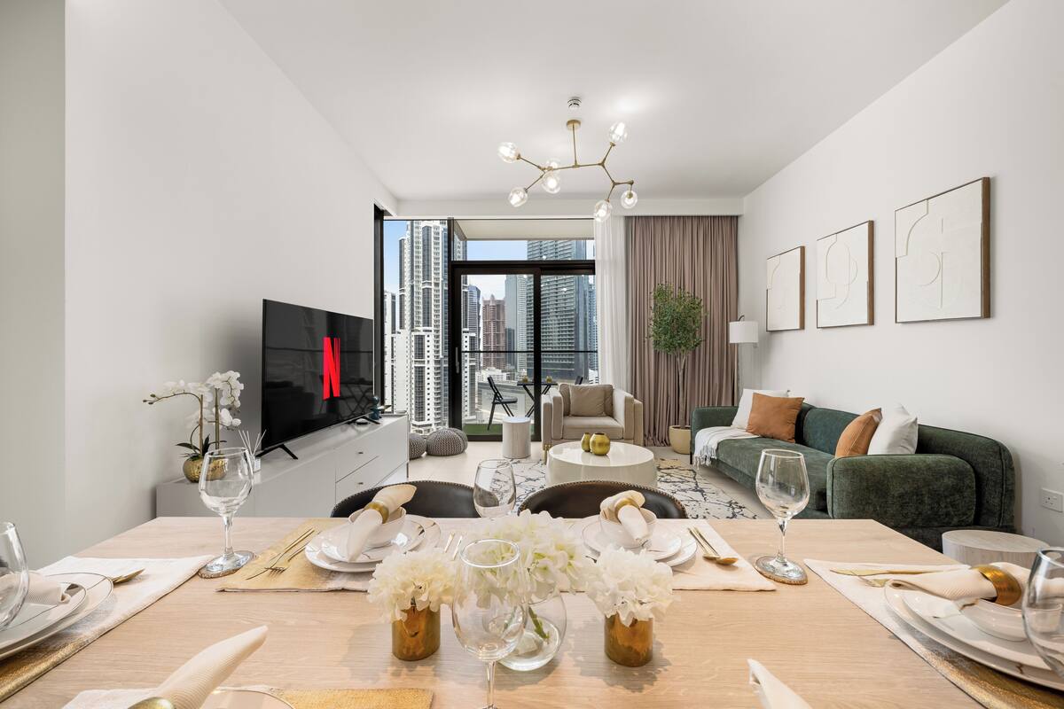 A modern living room with a dining area set for a meal, a television, and a city view.