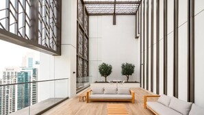 A spacious balcony with a modern design, featuring a wooden floor, a sofa, a small table, and two potted plants. - Delujo Stays – Burj Crown Collection (Dubai)