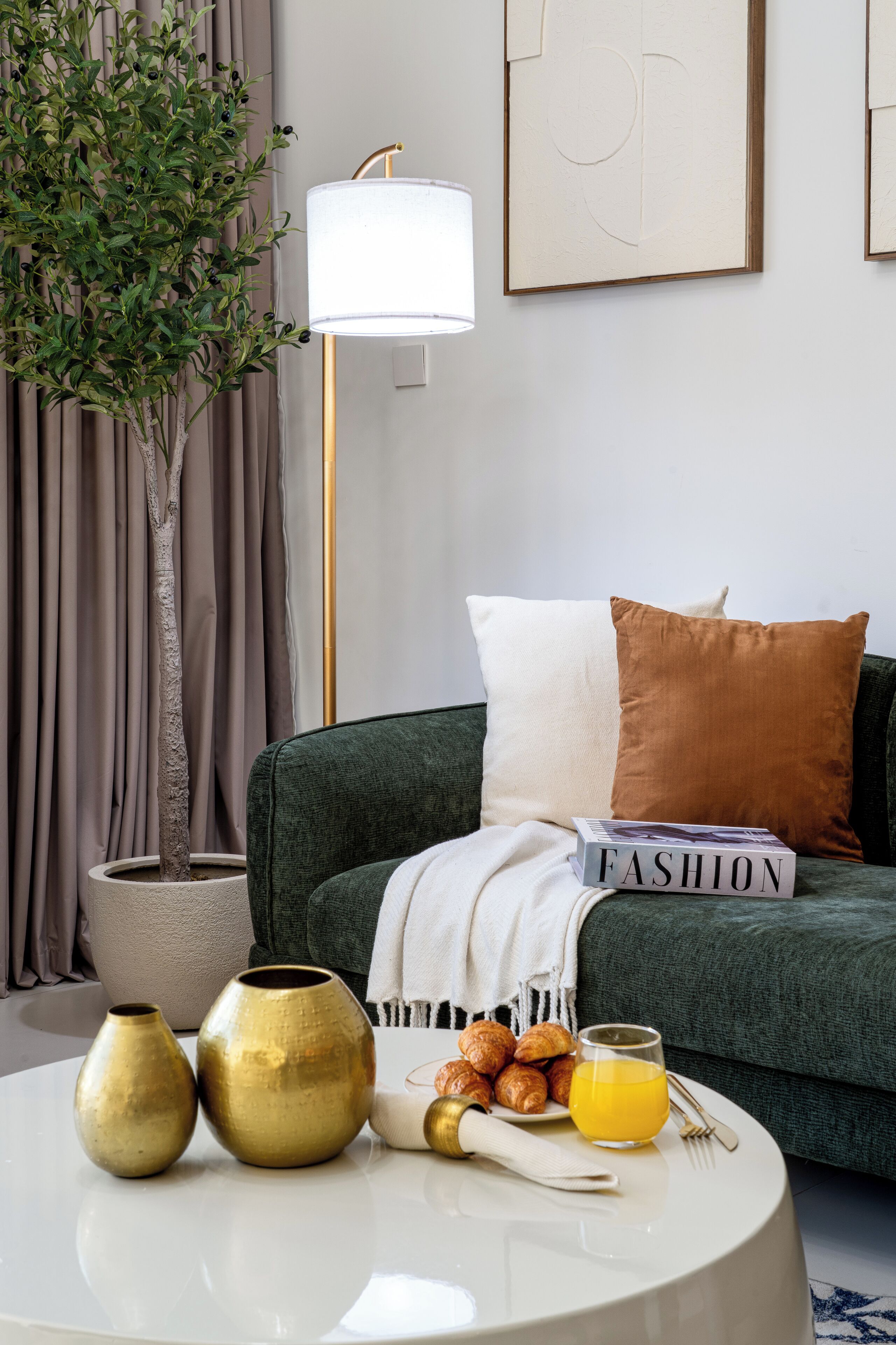 Un salon moderne avec un canapé vert, une table basse ronde agrémentée de vases décoratifs, une plante en pot et une lampe.
