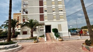 A multi-story building with a central entrance, surrounded by palm trees and a paved walkway. - Apartamento Torreblanca III Ref 063 (Torreblanca)