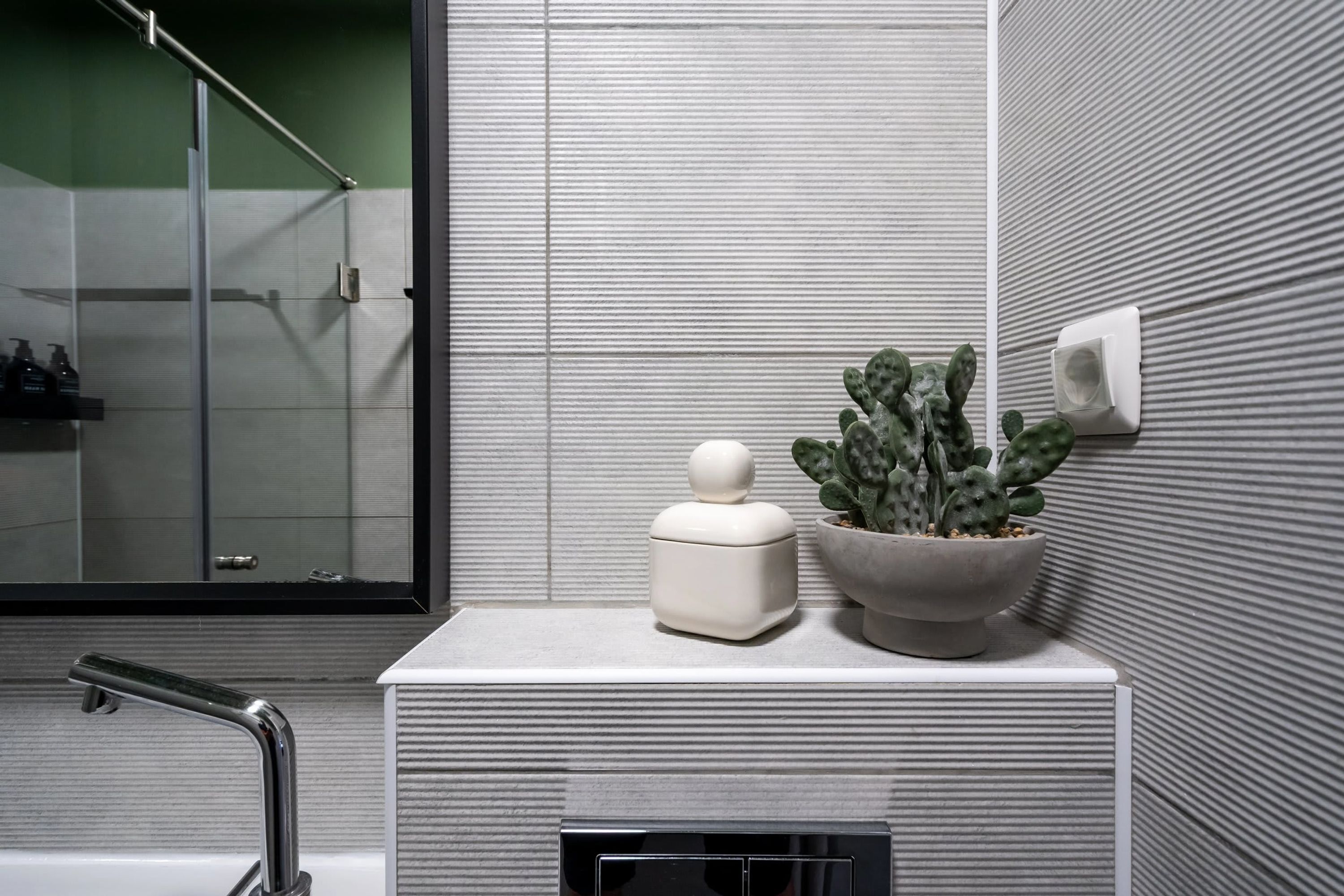 Une salle de bain moderne avec une douche à parois de verre, un lavabo blanc doté d’un distributeur de savon rond et un cactus en pot.