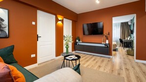 Ein modernes Wohnzimmer mit einer Couch, einem kleinen Tisch, einem Fernseher und einer Küchenzeile mit Esstisch und Stühlen.