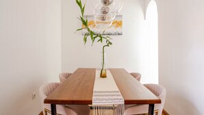 Un coin repas comprenant une table en bois, deux chaises, un luminaire suspendu et un tableau accroché au mur.