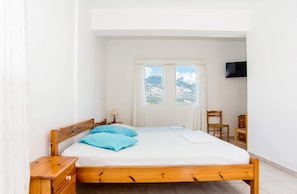 A bedroom with a wooden bed, a nightstand, a chair, a TV mounted on the wall, and a window with a mountain view.