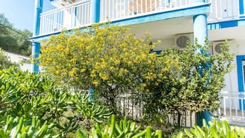 Um edifício com vários andares, varandas, aparelhos de ar condicionado e uma árvore com flores amarelas na frente.