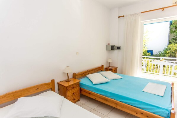 A bedroom with a wooden bed, a nightstand, a bedside table, a window with curtains, and a view of greenery outside. - Bluewhite Studio - Garden by the Pool (Kefalonia)
