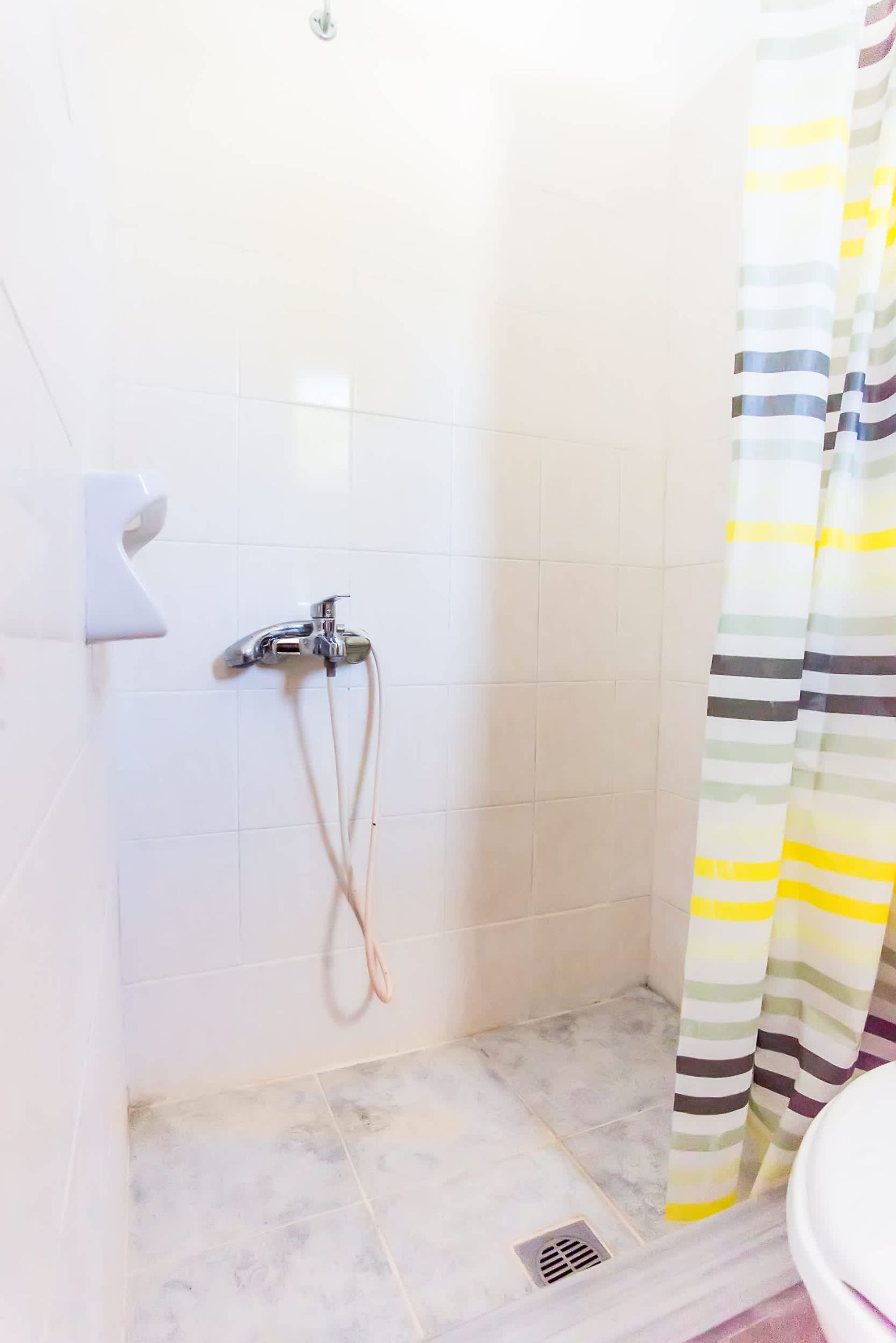Un petit espace de douche carrelé, équipé d’un pommeau de douche et d’un flexible, de toilettes et d’un rideau de douche à rayures.
