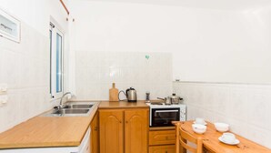 A compact kitchen with wooden cabinets, a sink, a microwave, and a small dining table with cups and bowls. - Bluewhite Studio - Garden by the Pool (Kefalonia)