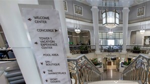A hotel lobby with a signpost indicating amenities such as a welcome center, concierge, vacation experience center, pool area, spa/boutique, marketplace, and sport courts.
