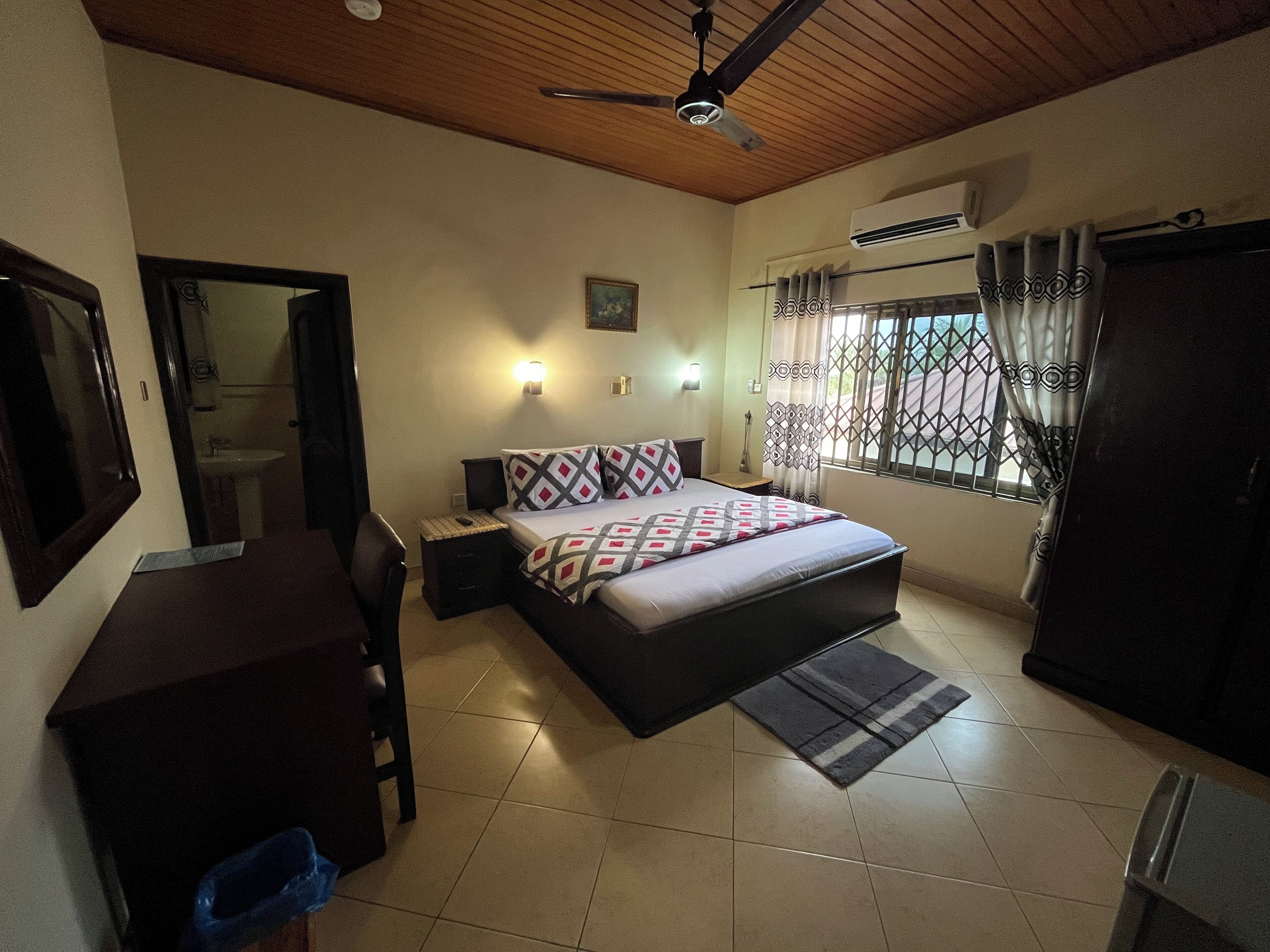 A bedroom with a bed, bedside table, desk, chair, and a ceiling fan.