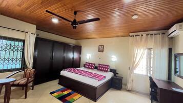 A bedroom with a bed, a desk, a chair, a ceiling fan, and a window with curtains.