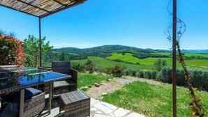 Eine Terrasse im Freien mit Korbmöbeln und einem Glastisch, mit Blick auf ein grünes Tal mit Hügeln.