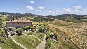 Ein Gebäude aus Stein mit einem Ziegeldach, umgeben von einem gepflegten Garten und einer hügeligen Landschaft im Hintergrund.