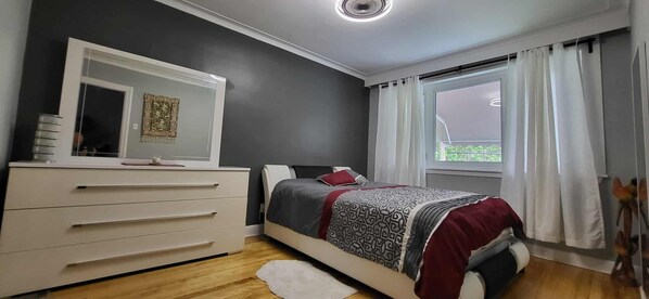 Een slaapkamer met een bed, een dressoir, een spiegel en een raam met gordijnen.