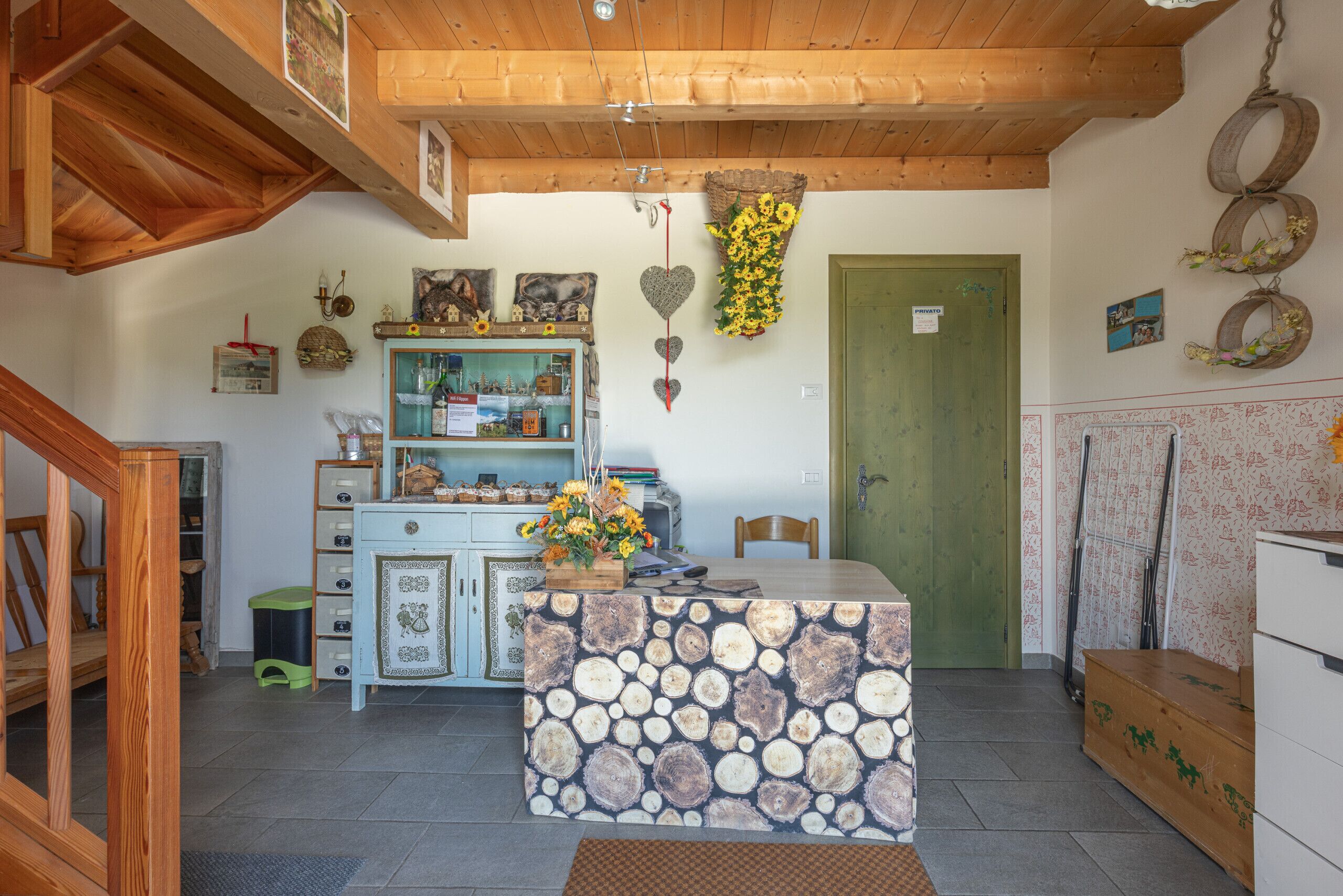 Une cuisine rustique avec un plafond en bois, une porte verte et un îlot central dont le plateau est décoré d’un motif évoquant du bois.