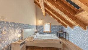 A bedroom with a sloped ceiling, a bed, a nightstand, a bedside table, and a window.